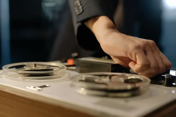 A close-up shot of a hand adjusting controls on a vintage reel-to-reel tape recorder.