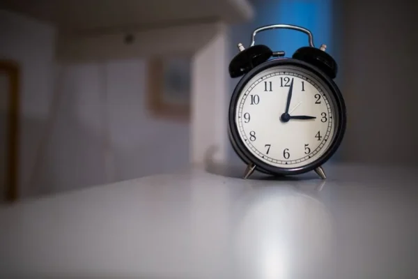 A classic black alarm clock with a white face showing 7:05, placed on a white surface.