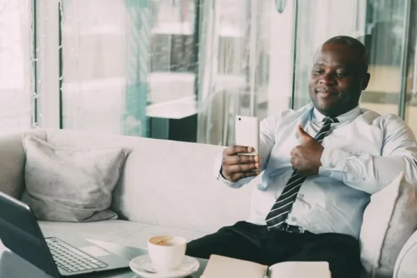 Confident businessman thumbs up during a video call in a relaxed office setting.