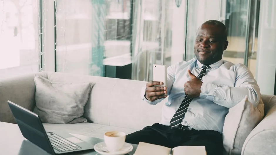 Confident businessman thumbs up during a video call in a relaxed office setting.