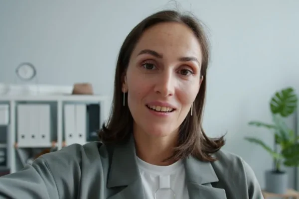 Close-up of a confident woman in an office environment, smiling at the camera.