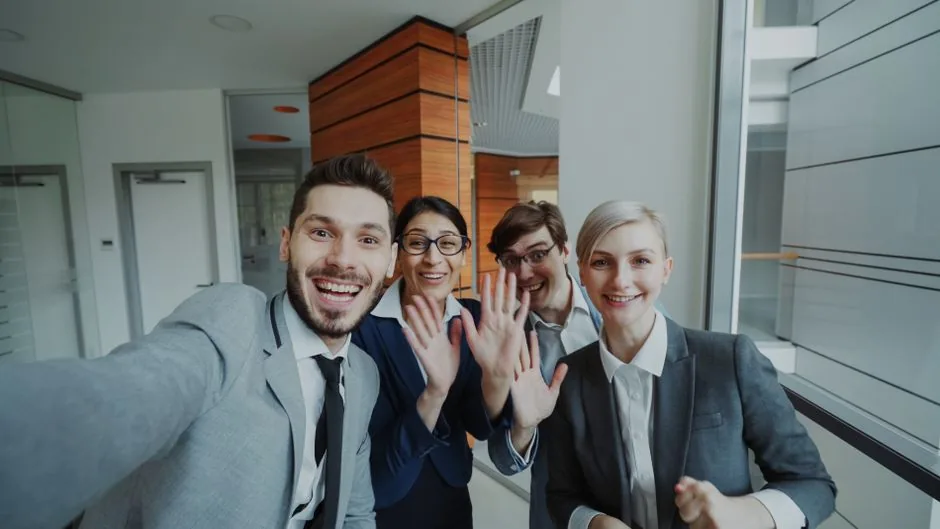 Cheerful business team smiling and waving at the camera indoors.
