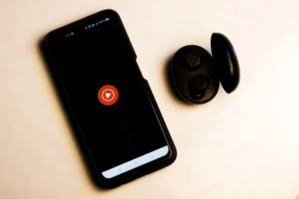 Flat lay of a smartphone and wireless earbuds on a neutral background, ideal for tech and lifestyle themes.