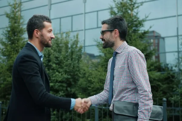 Two men shaking hands outside a modern office building, symbolizing business partnership.