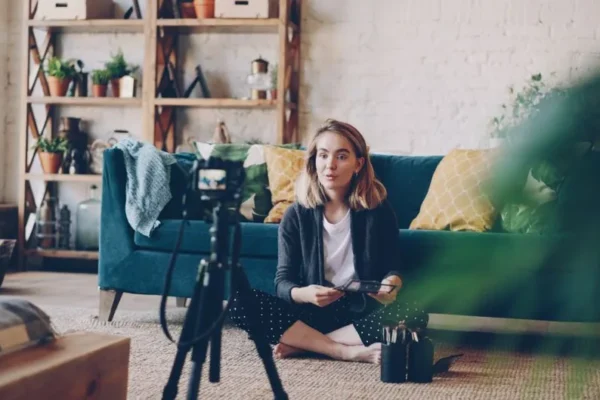 Woman filming vlog at home with camera setup, surrounded by plants and cozy decor.